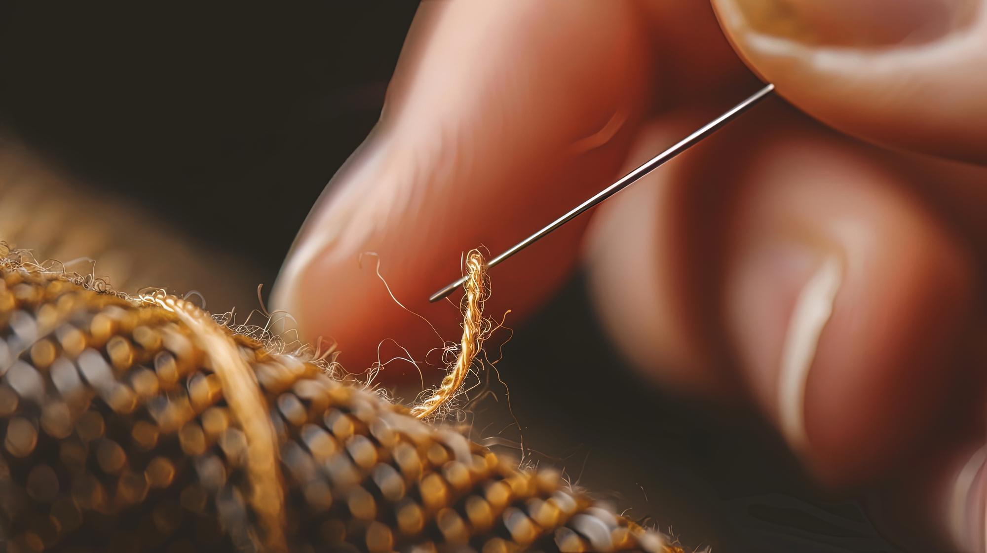 hand holding threaded needle over linen